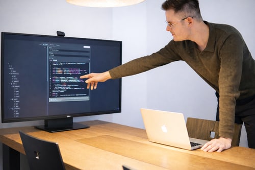 Mann zeigt auf Code auf einem Computermonitor.